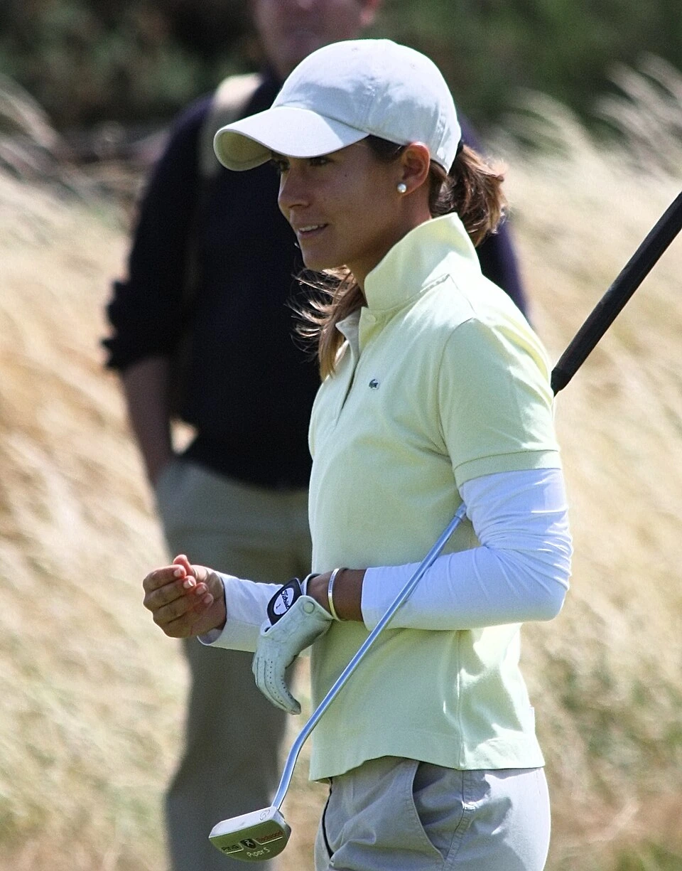 Azahara Muñoz on the golf course holding a club, wearing a white cap and light green shirt